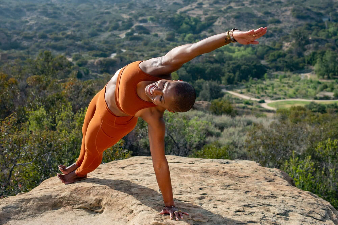 A Yogini in side plank pose on a sandstone rock. She wears a copper colored yoga outfit.  