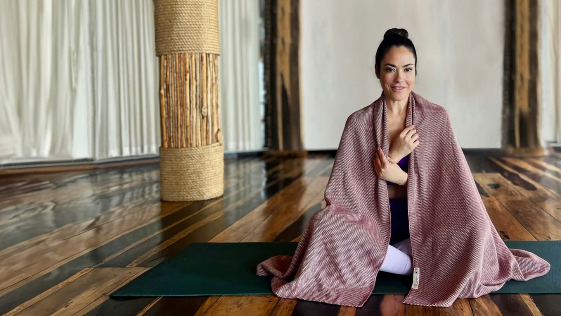 Yogi sitting on a yoga mat with the kinshe yoga towel made from 100% premium turkish cotton  in the colour garnet draped over her