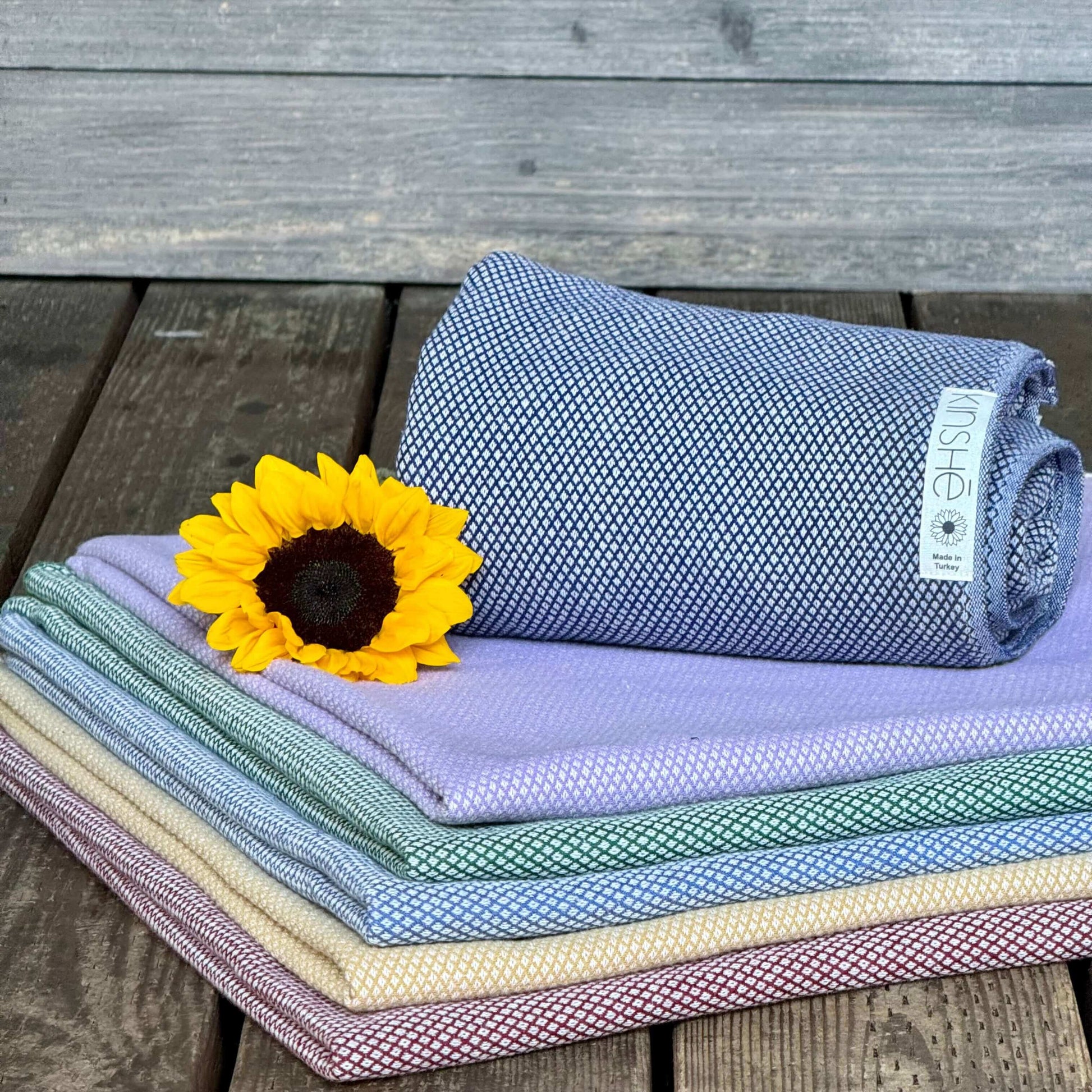 Kinshe Yoga displays their Premium Turkish cotton yoga towels gently folded near a sunflower. Subtle colors include Neptune blue, garnet red, turmeric yellow and forest green. Sold as the “Earthtowel,” it’s strong, soft and doubles as a meditation blanket